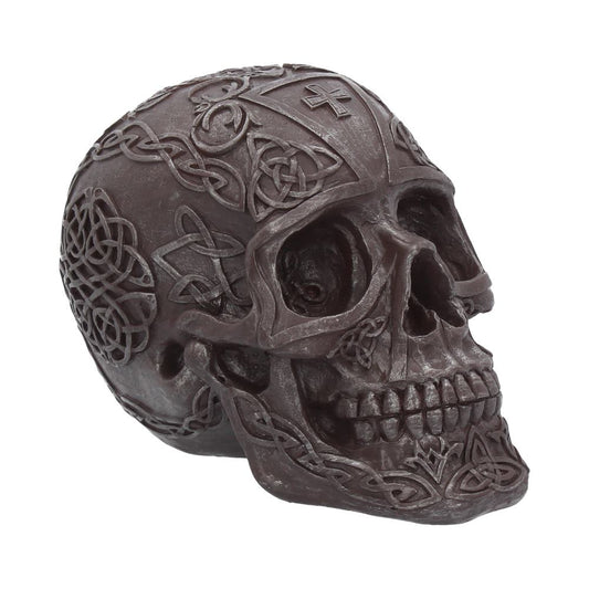A iron looking skull is on a white background. There is patterning all over it which is celtic in style and features a triqueta and a cross. The jaw sits forward and there are two rows of teeth on display.