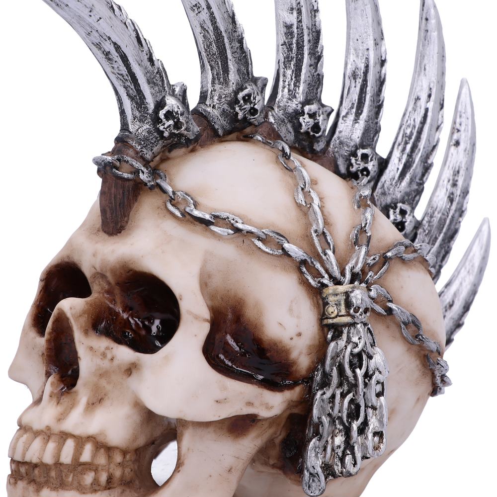 A close up view of a natural coloured skull ornament. You can see the deatailing of the silver coloured metallic blades of its mohawk. There are small skulls that are featured inbetween the blades and the chains that drape down the skulls head are clearly seen.