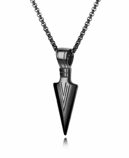 A plain white background is host to a hanging black arrow head pendant. The chain attached is the same colour and both are made from stainless steel. The arrow has patterned lines etched onto it and is shiny in appearance. 