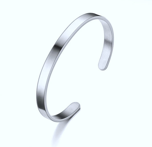 On a plain white background sits a narrow banded silver colour bangle style bracelet. It is plain in design and there is a gap in it where it can be slid onto a wrist.