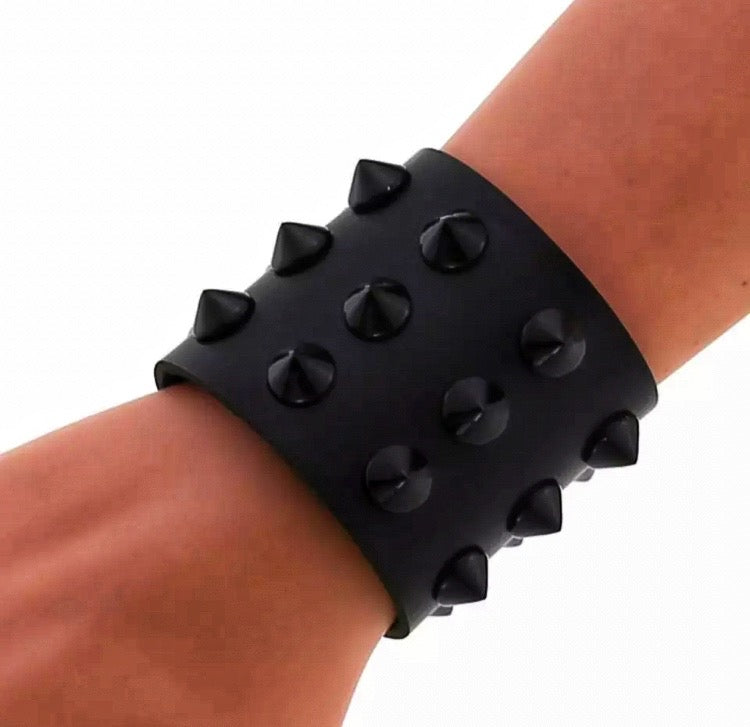 A wide cuff style bracelet sits on a wrist. There are spikes that go all around it which are in rows of 3. 