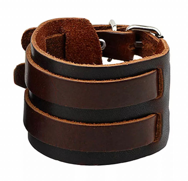 A brown wide leather cuff bracelet sits on a white background. On top of the wider part sits two narrower straps. 