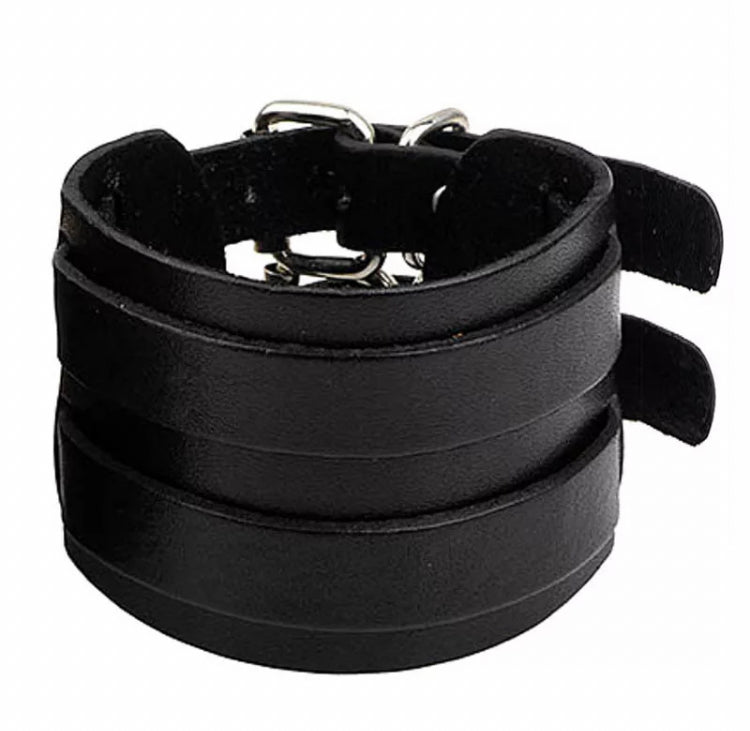 A wide black leather bracelet is on a white background. There are two smaller straps that sit on the main wider part and at the back you can just see the metal buckle that fastens it.