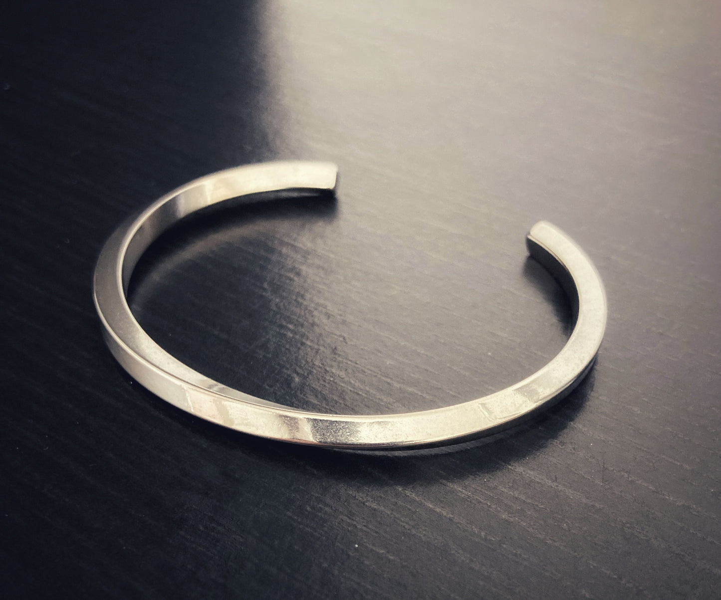 Lying on a black background is a bangle style bracelet that is silver coloured and lightweight to hold. The item has a twisted design that runs around it and an opening for putting onto a wrist