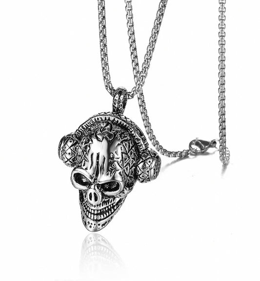 A white background hosts a silver stainless steel skull pendant attached to a sturdy looking chain with a metal clasp. The skull has exquisite detailing including a pair of headphones, sunken eyes and a demonic grin.