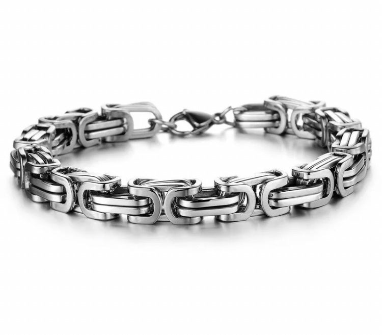 On a plain white background sits a silver coloured bracelet. This is made up of interlocking chains and is chunky but light in weight. There is a metal clasp that fastens the item and it is shiny in appearance.