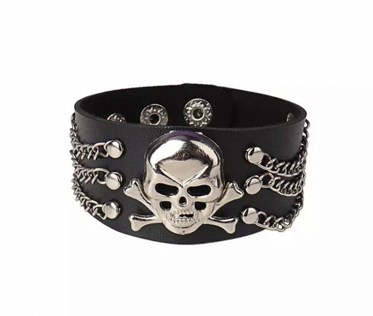 A wide black leather bracelet is on a white background. At the forefront of it is a skull and crossbones design with 3 chains at either side of this, all these are silver in colour giving the bracelet a good contrasting look.