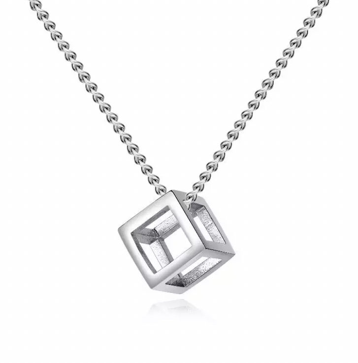 Upon a plain white backgrounds is a stainless steel cube pendant. This is on a solid looking chain and both items are silver in colour. The cube is a 3d style item that is hollow and not solid making it fairly light in weight.