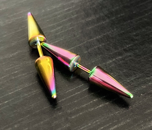 A pair of brightly cololured earrings sit on a black surface. They have a spike at either end of them with a small bar in the middle. They are shiny to look at and the light glistens off of them.