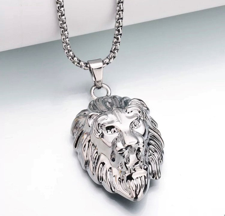 A white background is the setting for a shiny silver colour lion head pendant with chain. featuring a mane of hair engraved around the head and detailing to the face this is a stunning item.