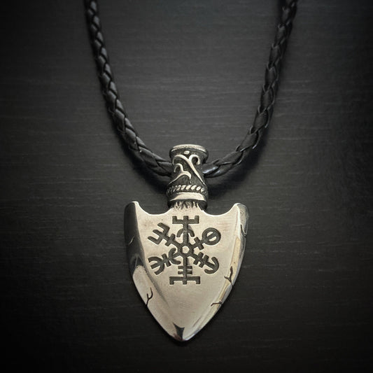On a thick black cord necklace sits a solid looking pendant. In the shape of an arrows head it is silver in colour and features a black engraving of a vegvisir design. There are also a few markings on it made to look like small cracks.