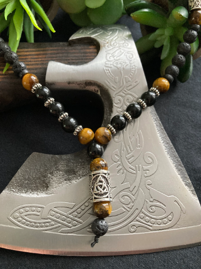 A necklace hangs over a axe blade. It features gold/yellow colour beads with dark streaks runnig through them and also black beads. There are also small metal pieces seperating some of the beads from each other.