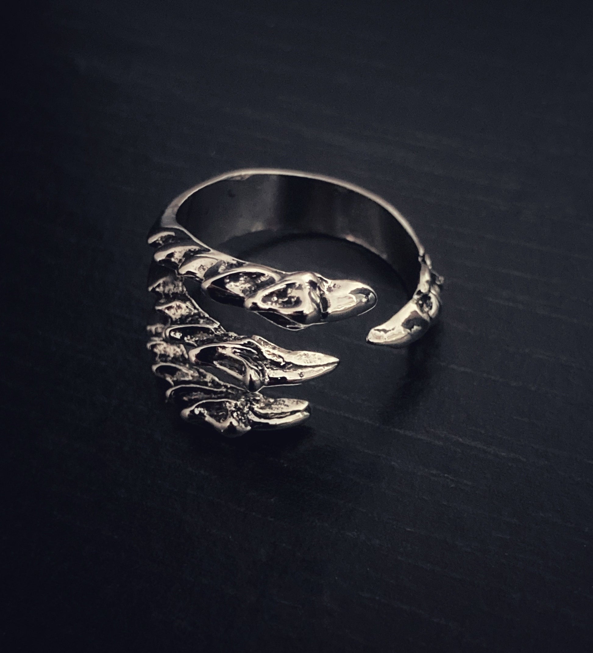 A side view of a dragons claw shaped ring. This has 4 claws in total with 3 one side then a gap before the other one allowing for adjustment to sizing. Engravings on the claws are on show which are intricate in their patterning.