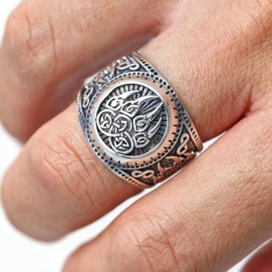 A close up of a hand is shown here with a ring on the middle finger. There is a circular design on the top of the ring which has a claw engraved onto it. You can just see the intricate pattening that sits on the side of the ring itself.