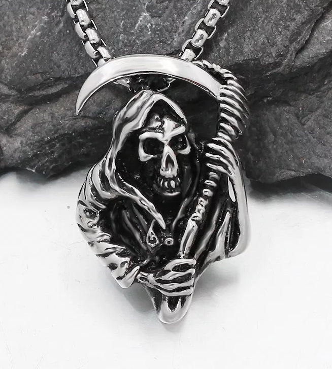 leaning against a rock is a necklace in the shape of the grim reaper. Holding a scythe above its head and wearing a cloak the features of this item are detailed and precise. Attached to a chain the whole piece is silver in colour and solid and chunky