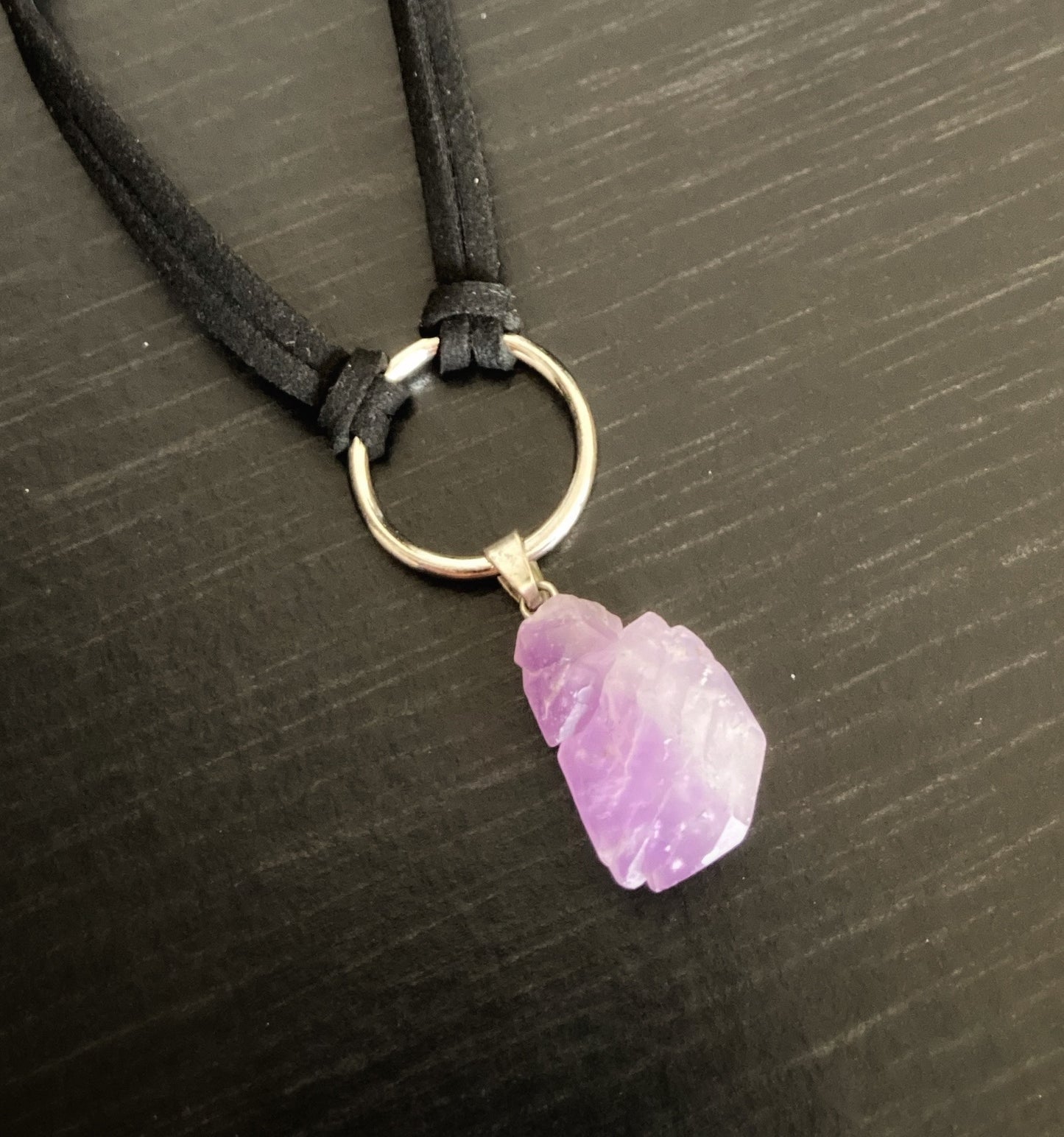 A purple colour crystal is attached to a ring in a silver colour. There is then a black cord tied to that as the necklace part of a choker.