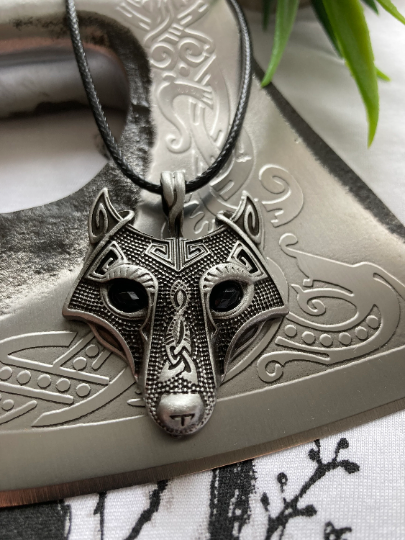 A close up view of the wolf's head pendant that is featured here lying on an axe blade. The stunning detail including the all the engravings on the face are on display and can also be felt when touching the item. 