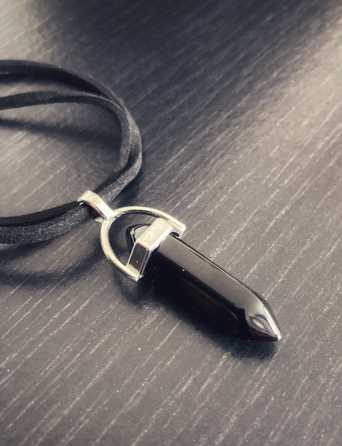 Two black bands are holding a black healing stone pendant which is held on with a silver coloured holder. The whole thing is lightweight and the healing stone glistens in the light.