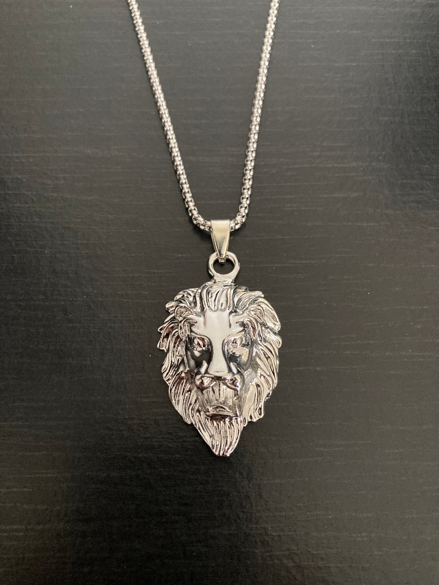 A front view of a stainless steel silver coloured chain with lion head pendant attached to it. With detailing on the face and mane this item is shiny in appearance and quite light to hold.