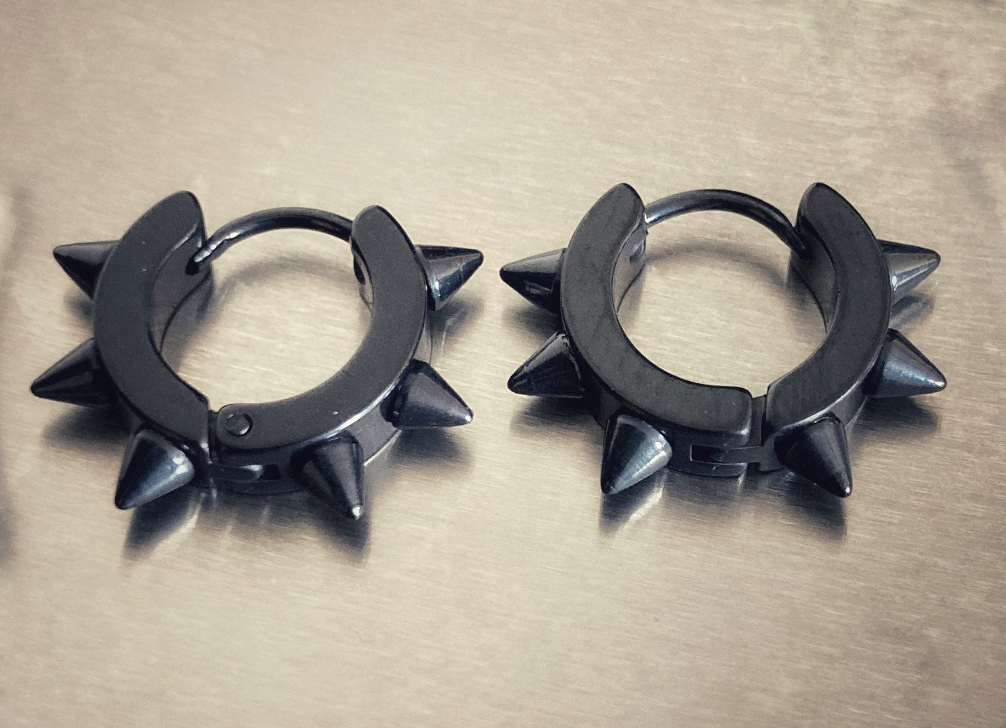 A pair of ring shaped earrings with spikes attached to the outer rim. Black with a thin sleeper style bar that opens for attaching to your ear.