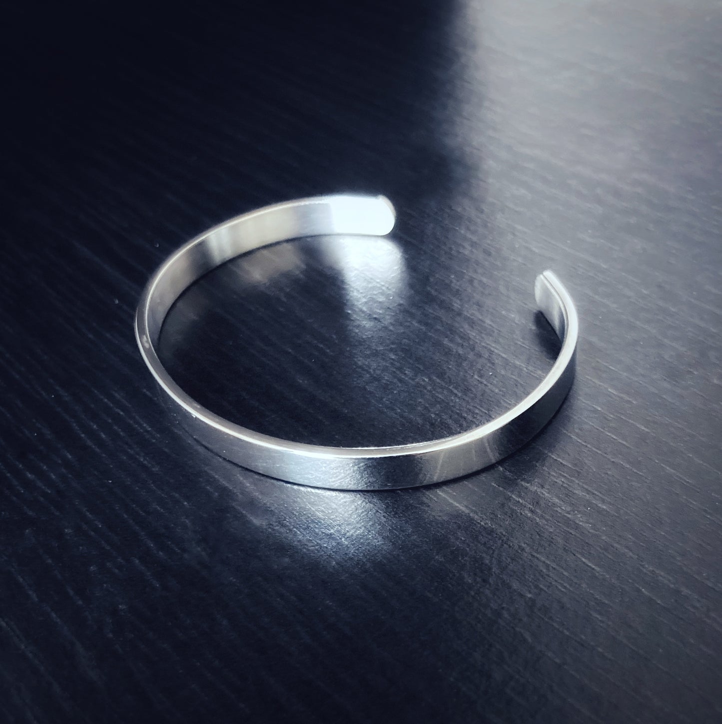 A bangle style bracelet is on view that is silver in colour and has a shiny look to it. It is narrow and is plain and is lightweight to hold and wear.