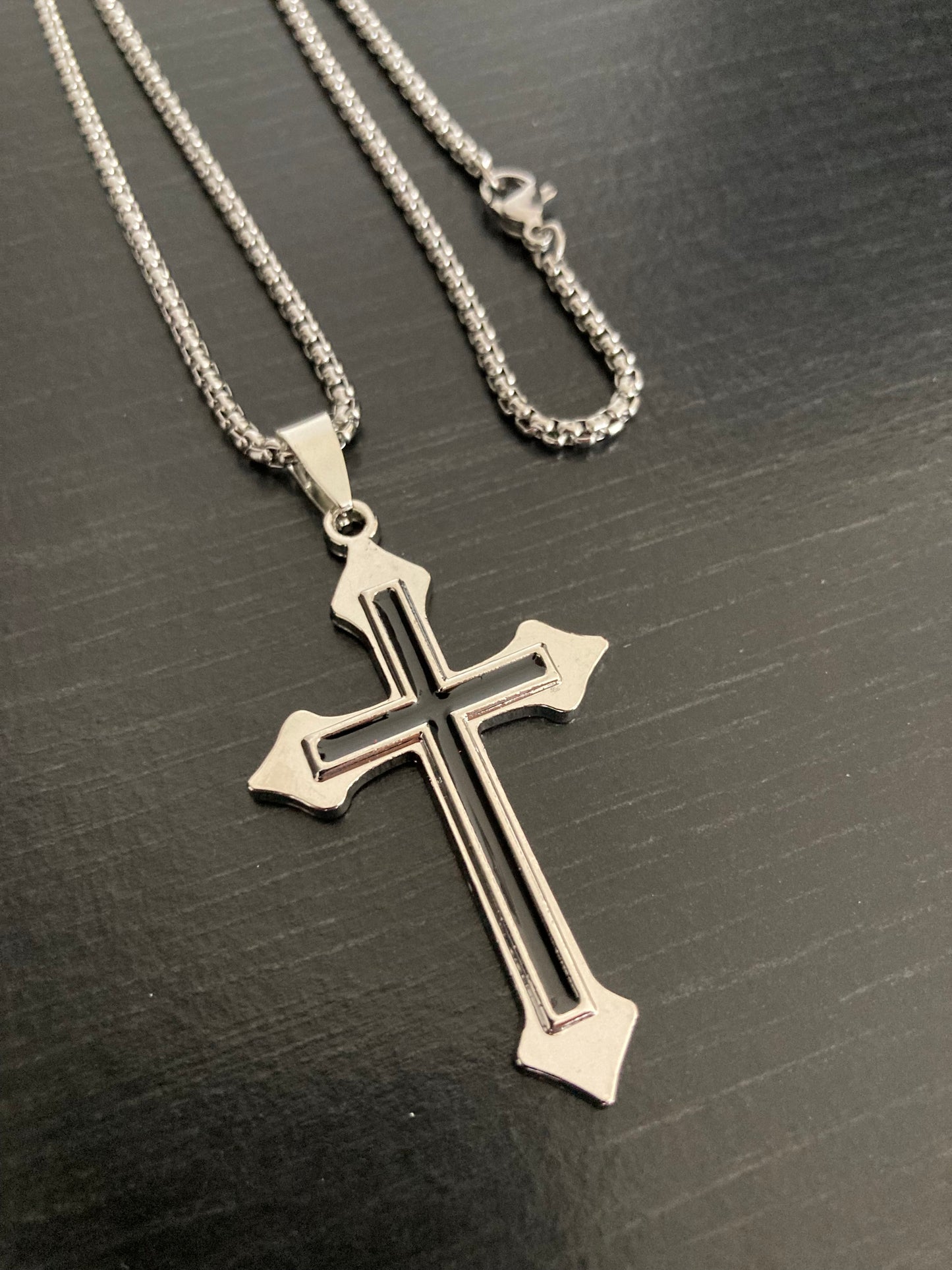 A chunky looking cross pendant is attached to a chain with a metal clasp for fastening. The pendant is 2 crosses on top of each other but different sizes and colours.