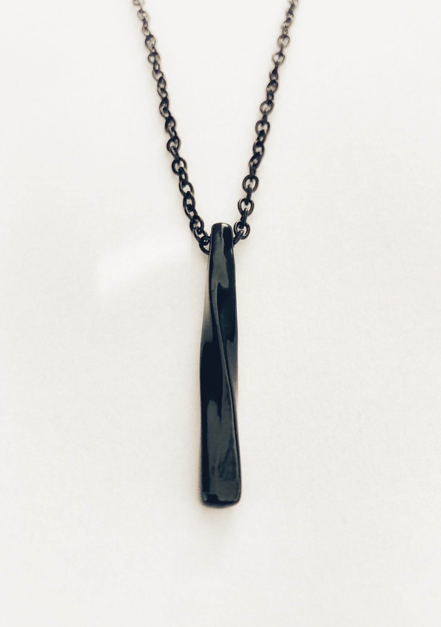 A long twisted bar shaped pendant is dangling from a chain. Both are black in appearance and the pendant is lightweight to hold.