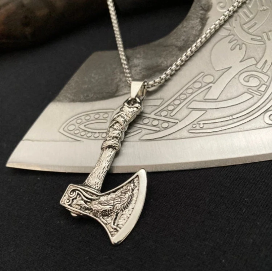 Sitting on a patterned axe blade is a stainless steel pendant in the shape of an axe. There is a wolf design etched onto the main part of the head and the bottom of the hadle is textured to look like the leather on a real axe handle.