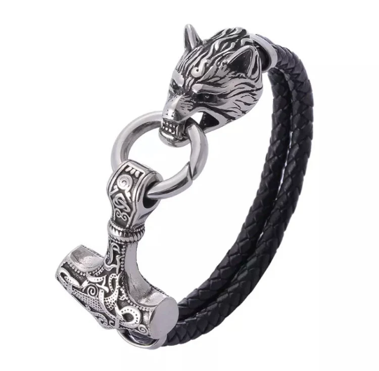 A plain white backgrounds hosts a view of a chunky looking black leather bracelet. There is a solid silver colour wolf head one end with a ring in its mouth. The other side of the ring holds a hammer shape which has an intricate pattern on it.