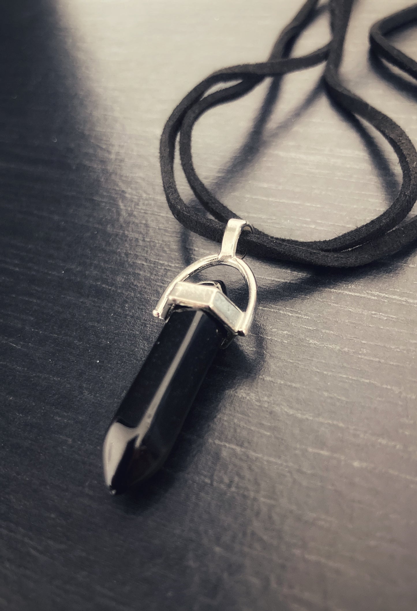 A black chakra healing stone is attached to two black cords making it a double banded necklace. The cord looks to be of strong material and the stone is shiny in appearance.