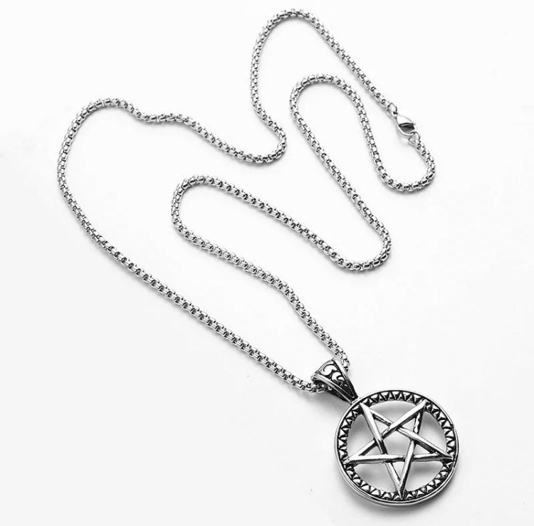 Upon a plain white background lies a silver coloured necklace and chain. The pendant is circular in shape with an etched pattern ring around the outside and a pentagram that is a cut out shape in the middle of it.