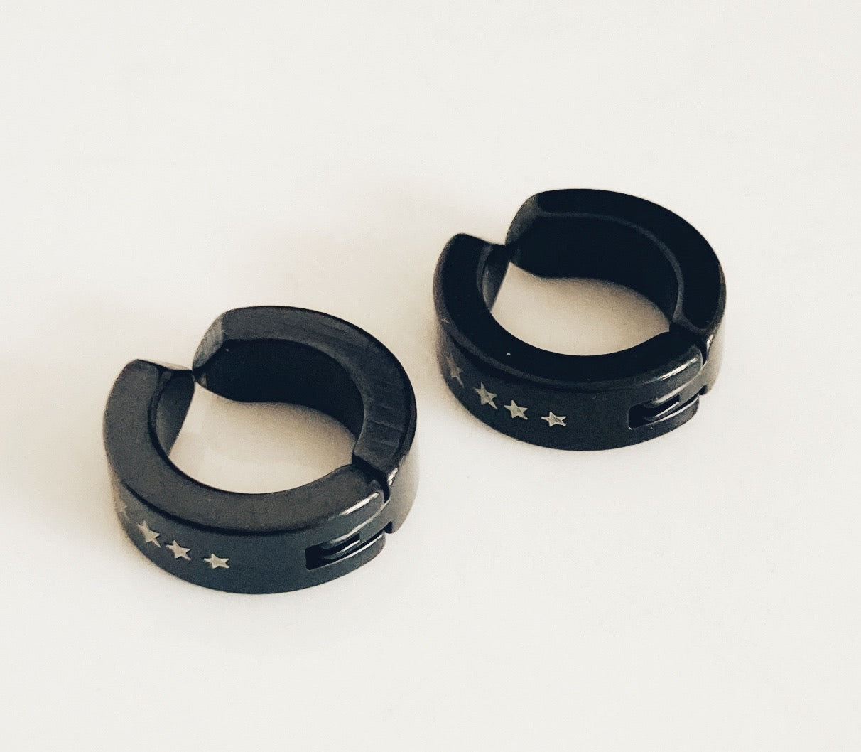 Two identical earrings sit side by side on a white surface. Small white stars are seen printed onto the black round earrings. You can see the join where the items open out. 