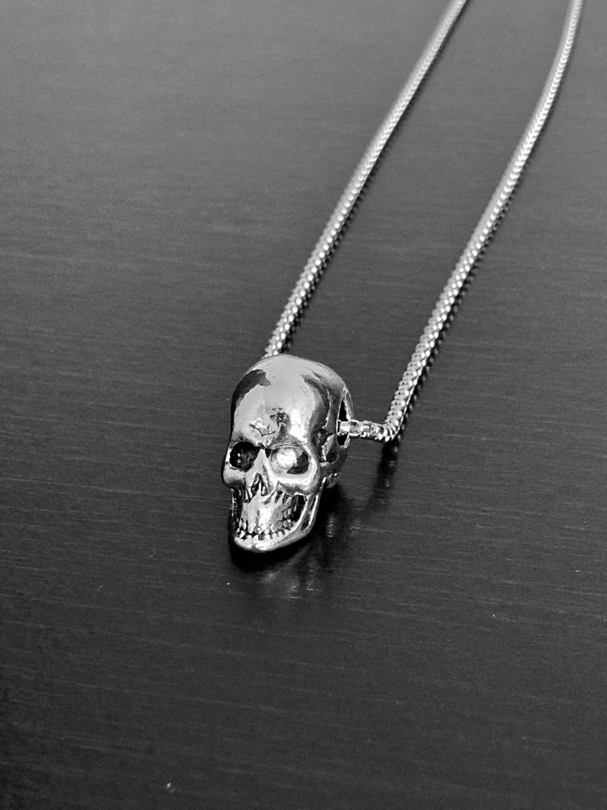 A sturdy looking chain holds a solid skull head pendant. Both are silver coloured and stainless steel. The skull has detailed features including sunken eyes, a wide grimace and cracks in the skull. This is a chucky but not too weighty item.