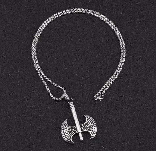 A view from above of a viking style 2 headed axe necklace. This shows the length of the stainless steel chain with a clasp and also a full view of the pendant. The heads of the axe are identical and have a raised pattern similar to dots on them.