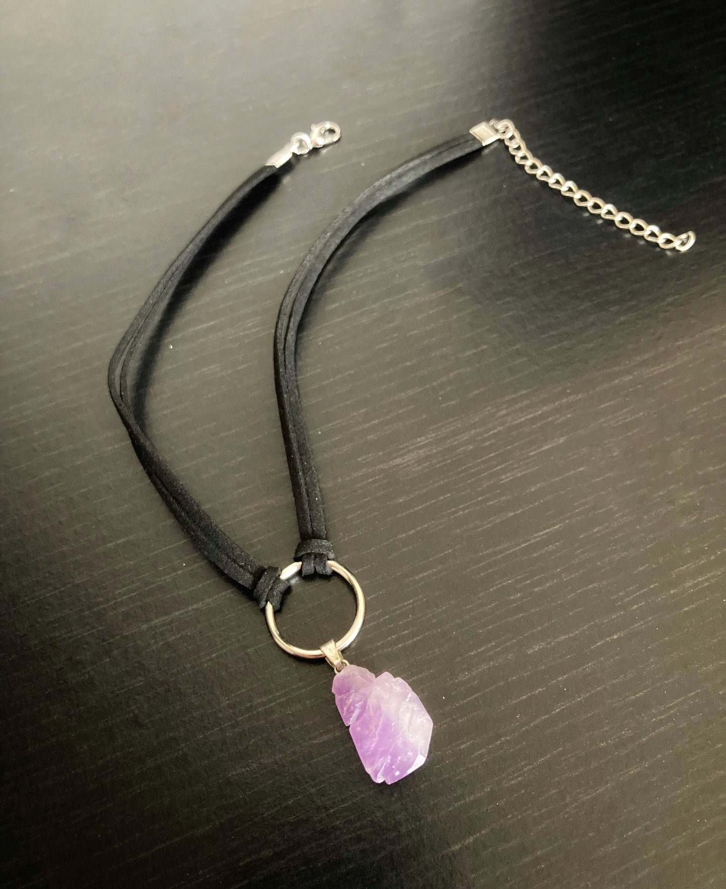 A full view of a black cord with metal clasp for fastening with a purple coloured crystal tied to it.