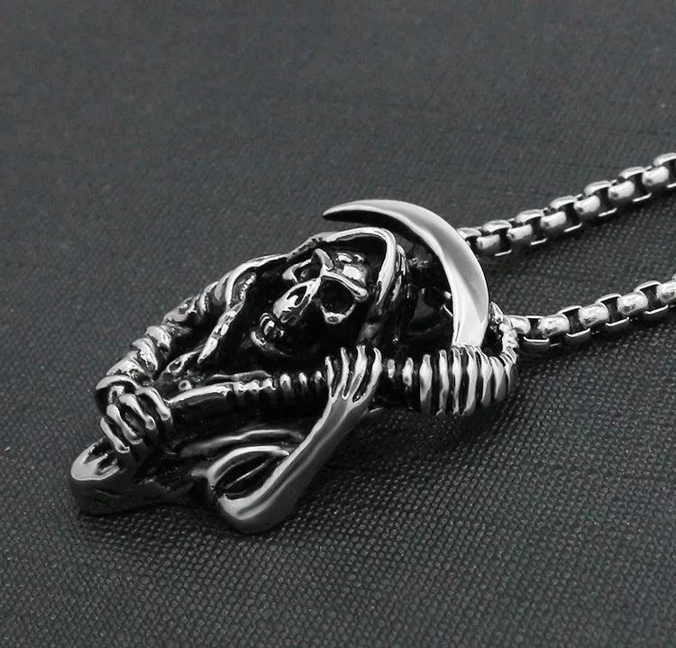 A grim reaper pendant is lying on a grey material surface. You can see the detailing close up of this item which is intricate in design. When you hold it you can feel the weightiness of it and the quality of the silver stainless steel.