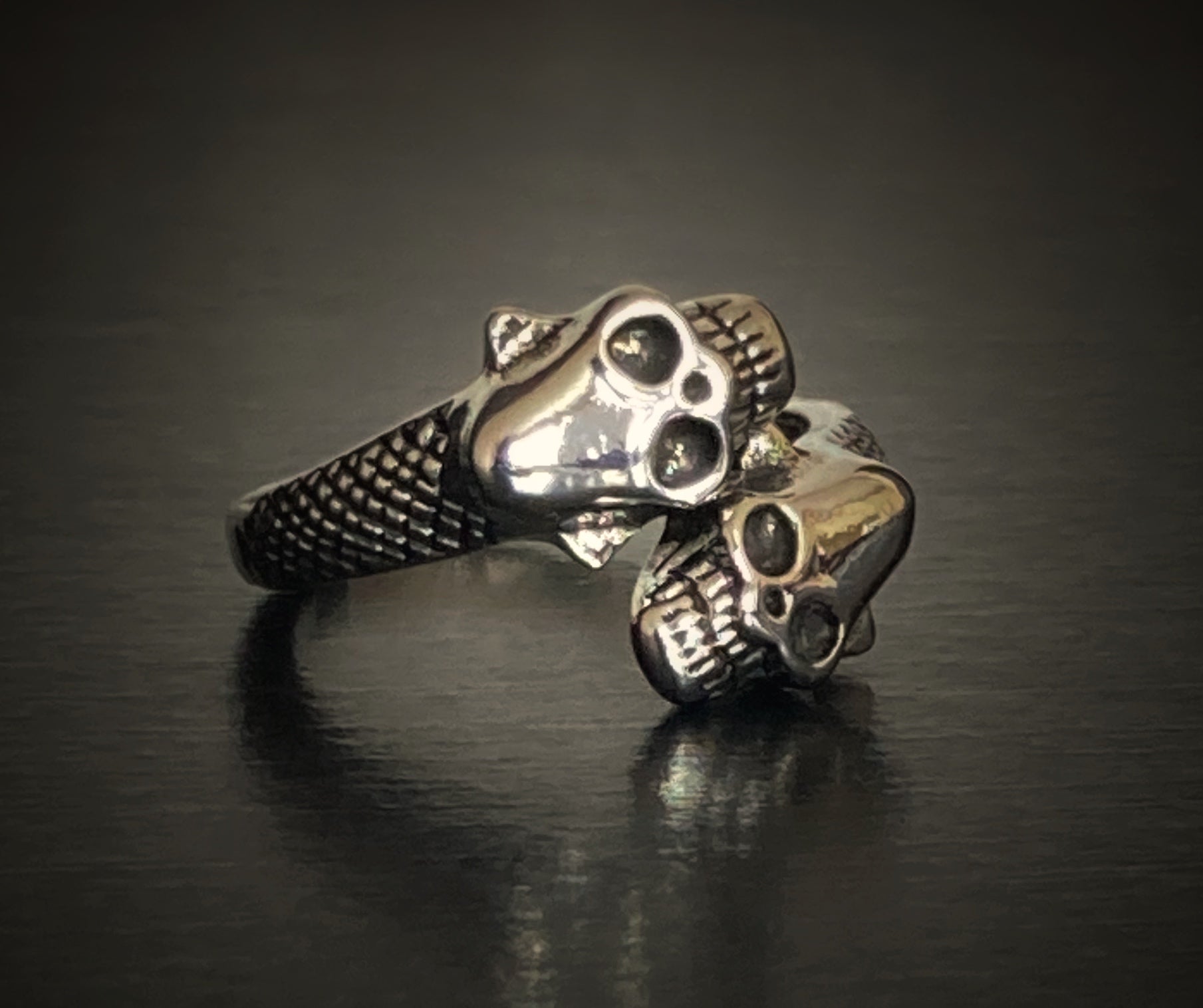 A close up view of a 2 headed skull ring. The skulls are detailed in their facial features and either side of the heads the ring has some intricate patterning.