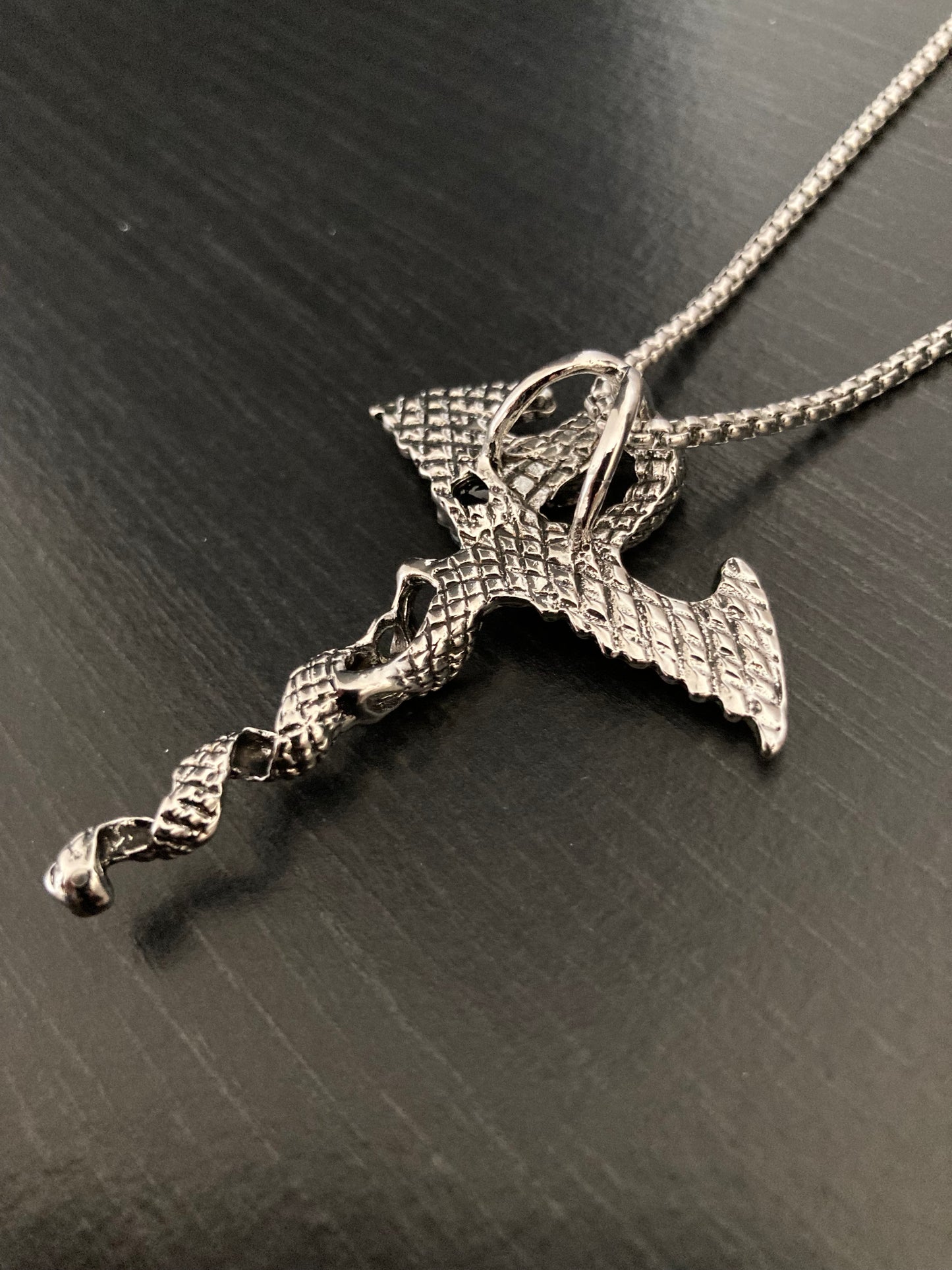 The reverse side of a dragon pendant neckalce. The chain can be seen attached to it and this looks and feels to be high quality. The back of the dragon itself has a detailed pattern all over it which can be felt when touched. 