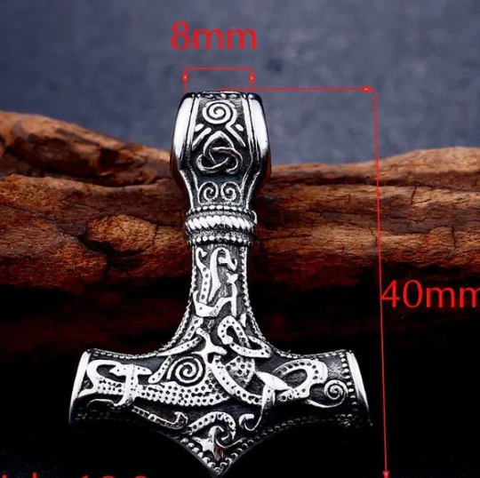 A piece of wood props up a solid shiny looking Thor's hammer pendant. This is a close up of the item and you can truly see the detailed pattern that runs over it. There is also a scale showing the size of it which is 8mm wide and 40mm long.