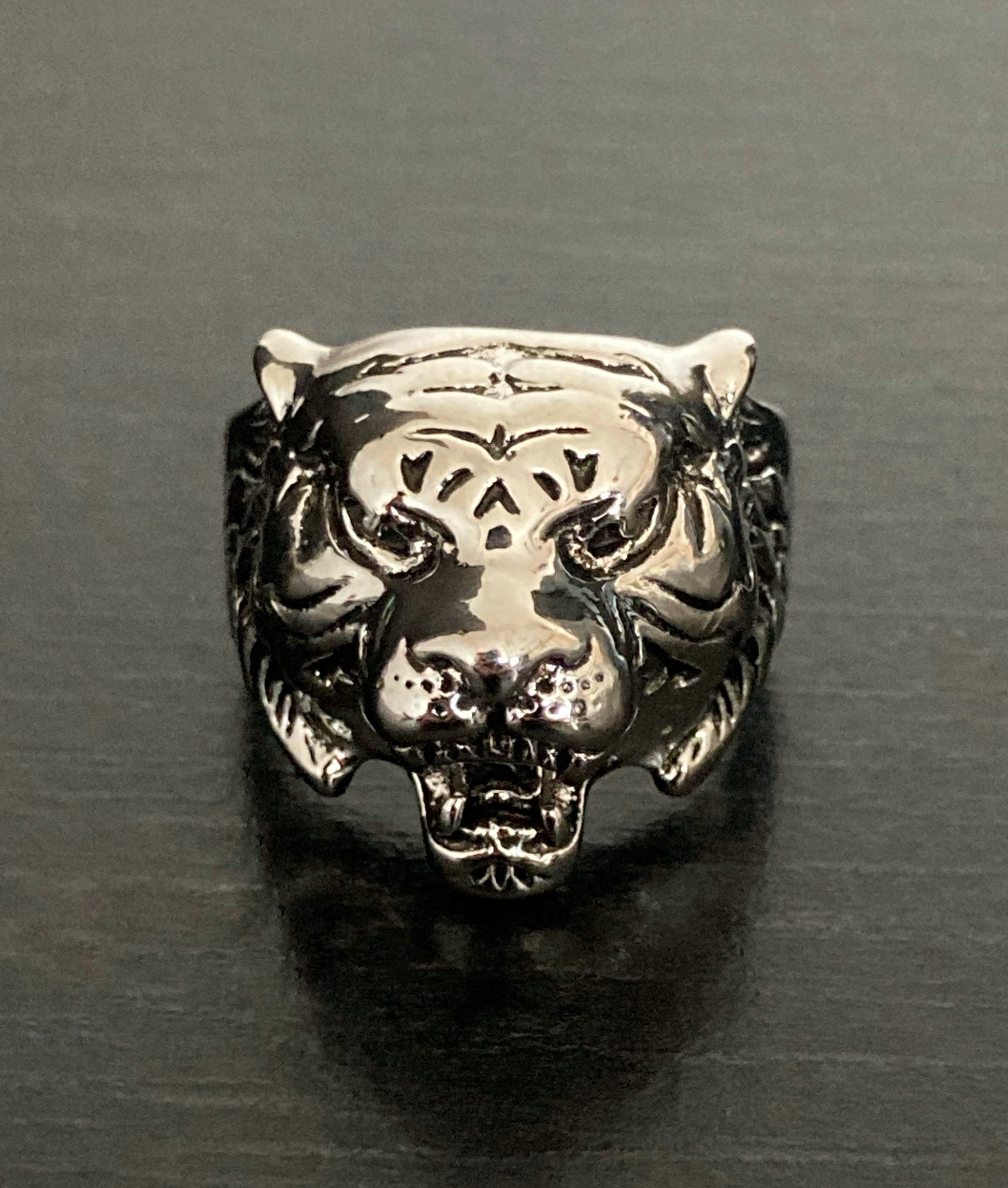 On a black background sits a ring in the shape of a tigers head. You can see close up the detailing on the face of this with its mouth open and ears pinned back. Silver in colour this is a solid piece of jewellery.