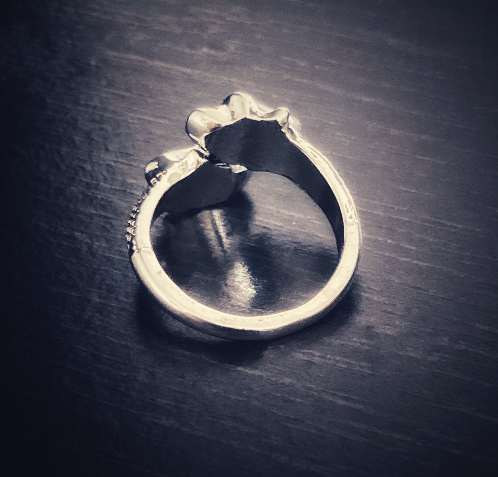 A back view of a silver coloured ring. A narrow band makes up the part that slides onto your finger and the two skulls move making this an adjustable ring. It is plain inside of the ring with the skulls being hollow inside.