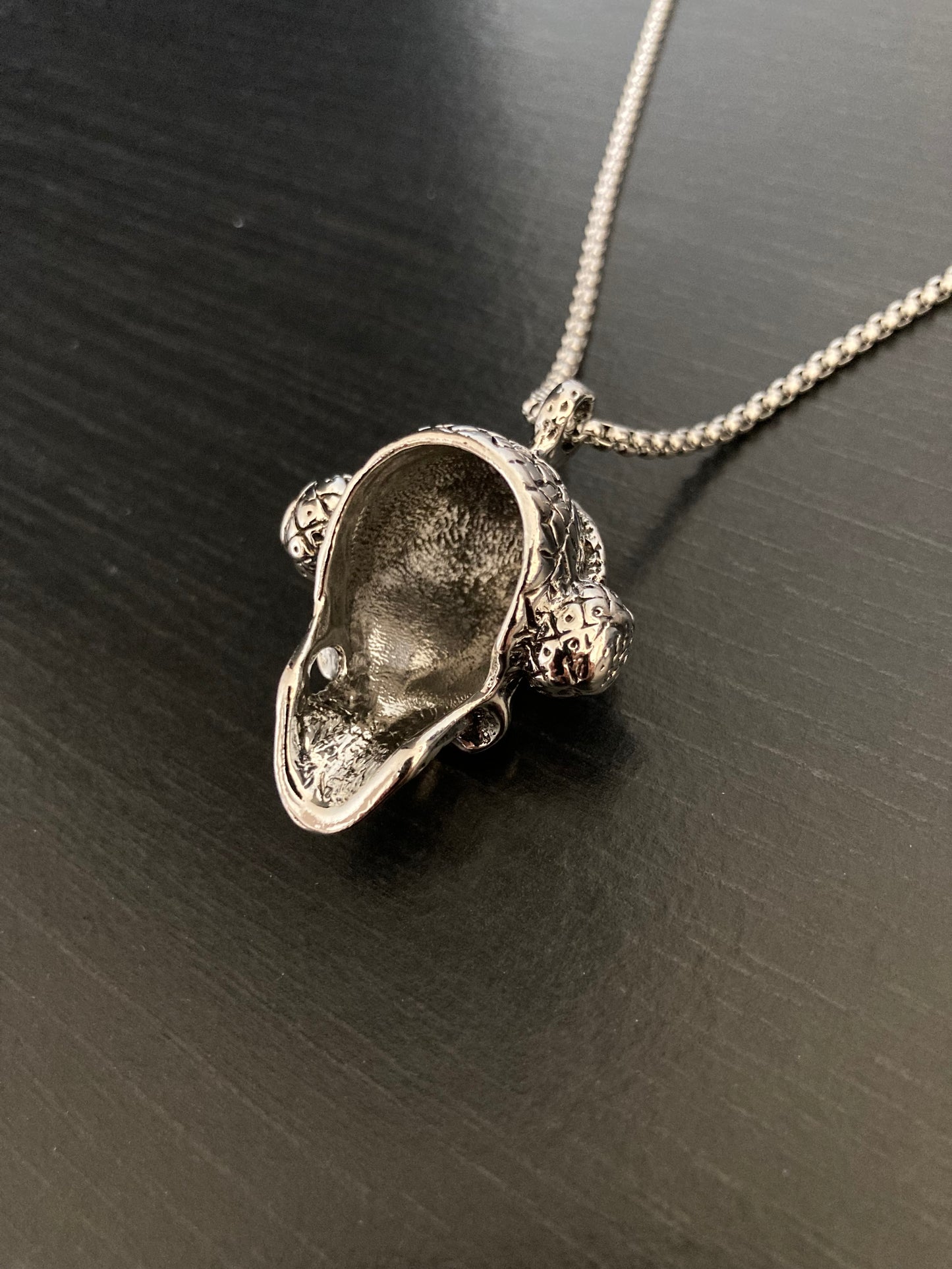 The rear view of a skull pendant which shows the back to be hollow and plain in design. You can see the sturdy looking chain which holds the skull and both are of good quality.  