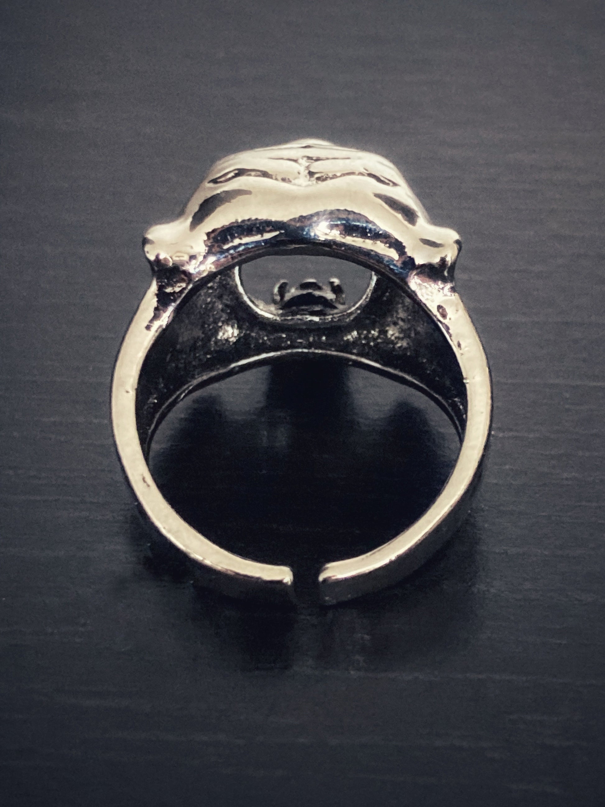 The rear view of a solid looking tiger head ring. There is a narrowish band that has a gap in the metal making it adjustable for the finger and it is plain inside and at the back of it. 