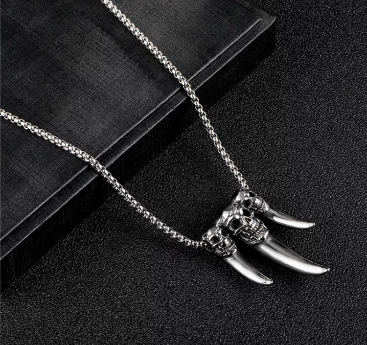 A chained necklace holds a pendant of 3 fangs. There are skulls carved onto fangs and these are menacing in appearance with beeth baring. The fangs are solid looking and slightly shiny.