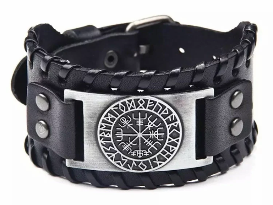 A plain white background with a black leather wide bracelet sitting in the forefront. There is a silver metal plate at the front which features a viking compass engraving in a circle surrounded by rune symbols. The bracelet looks high quality.