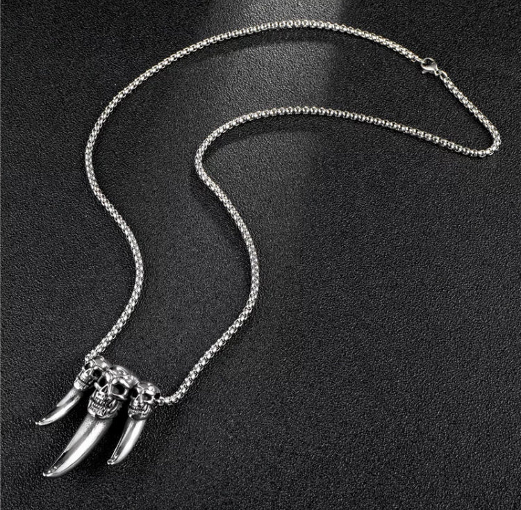 Attached to a pendant is a silver coloured chain with a clasp for fastening. The main feature is 3 fangs which are attached to the chain through the sides of a skull which is carved onto the top of each fang.