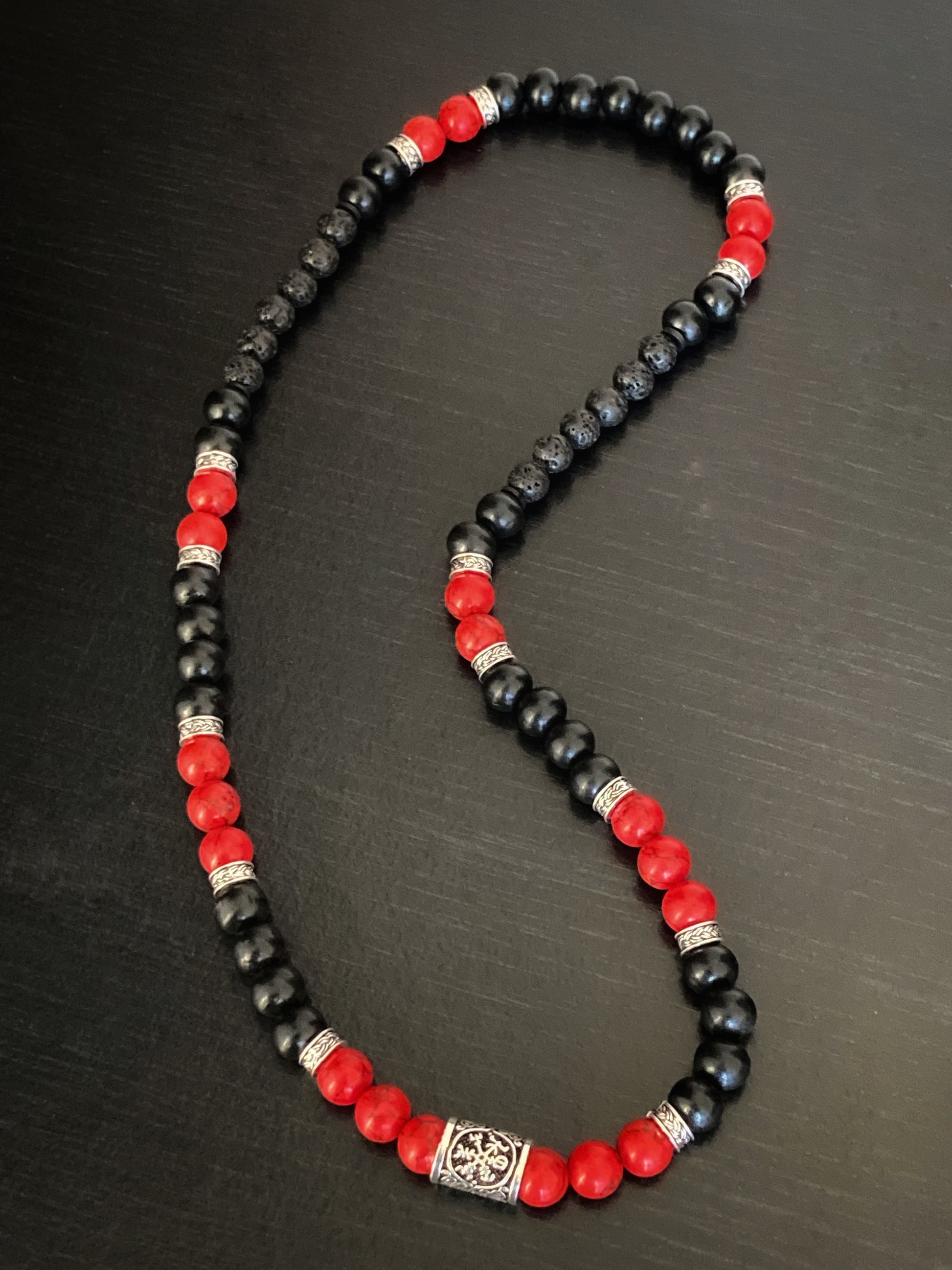 A view from above of a red and black beaded necklace. You can see the light glistening off of the beads themselves and to hold this necklace is weighty but not heavy. 