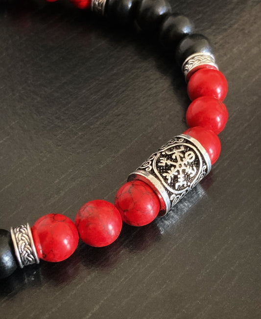A close up of a beaded necklace featuring red gemstone beads and black wooden ones. On show is a silver coloured metal rune with the compass vegvisir engraved onto it.