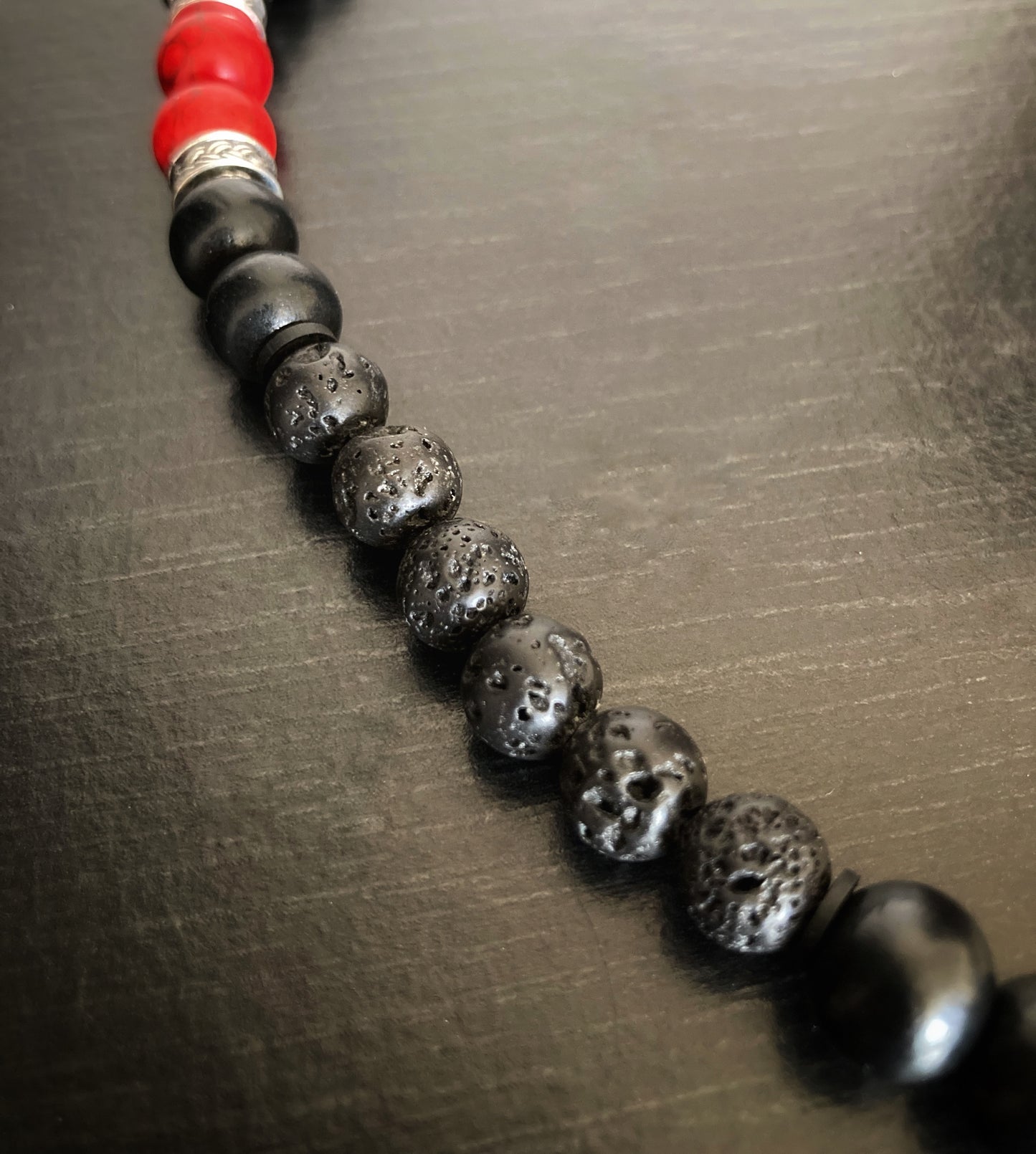 A close up of a section of a necklace that shows black lava style beads next to black wooden beads. The lava beads look more textured and are more of a matt black then the wooden ones which have a shine to them.