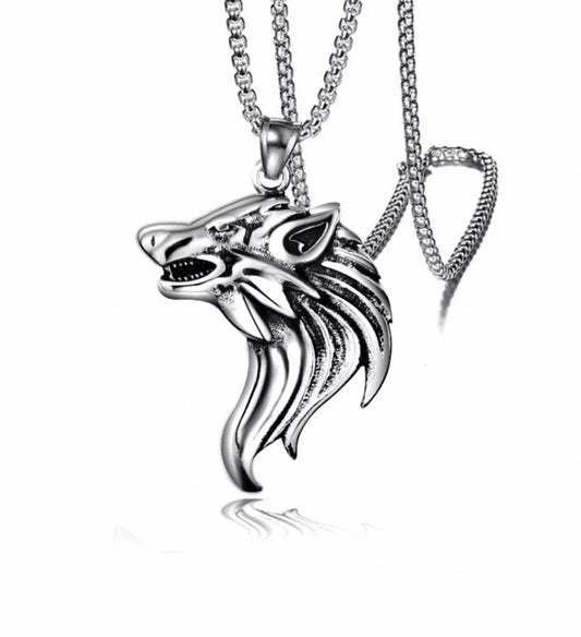 A plain white background with a ferocious looking wolfs head pendant on it. Stainless steel and silver in colour as is the chain attached to it. The wolf itself has stunning details on the face with a mane of fur running down behind its head.